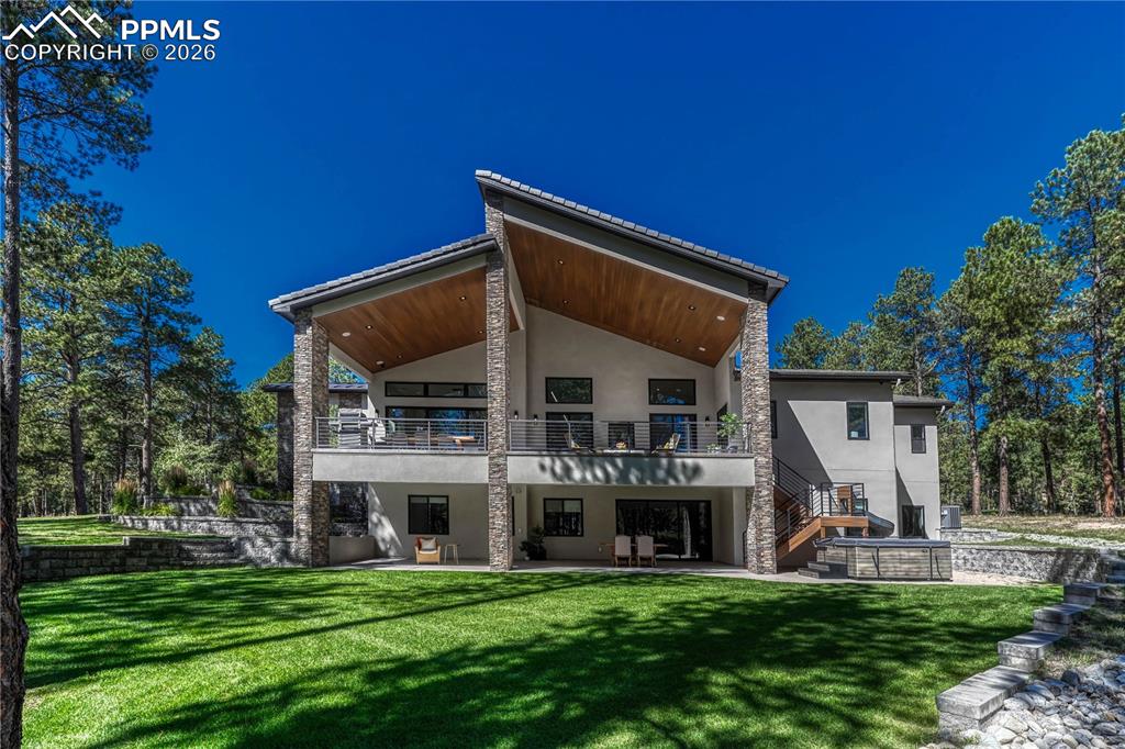 Back of property featuring stucco siding, a patio area, a lawn, and a balcony