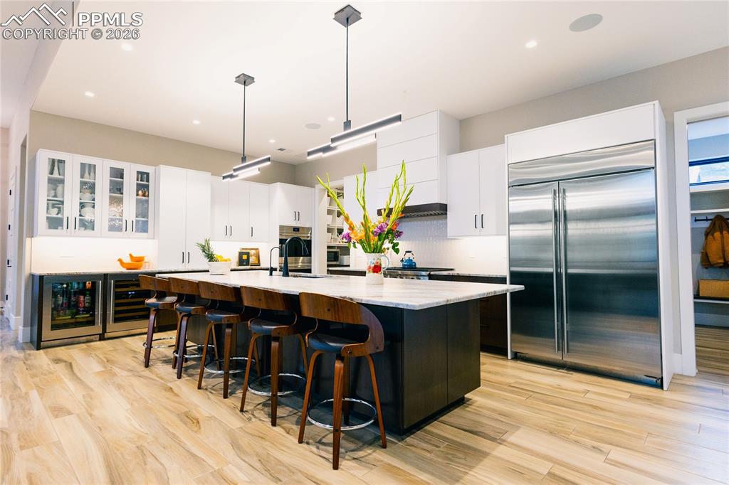 Two tone kitchen with two tone cabinetry, stainless steel appliances, a large island, decorative light fixtures, and a kitchen breakfast bar