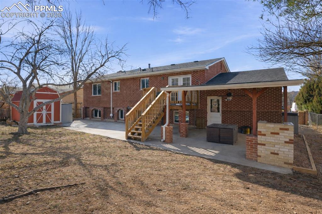Back of house featuring a storage shed, a patio, and brick siding