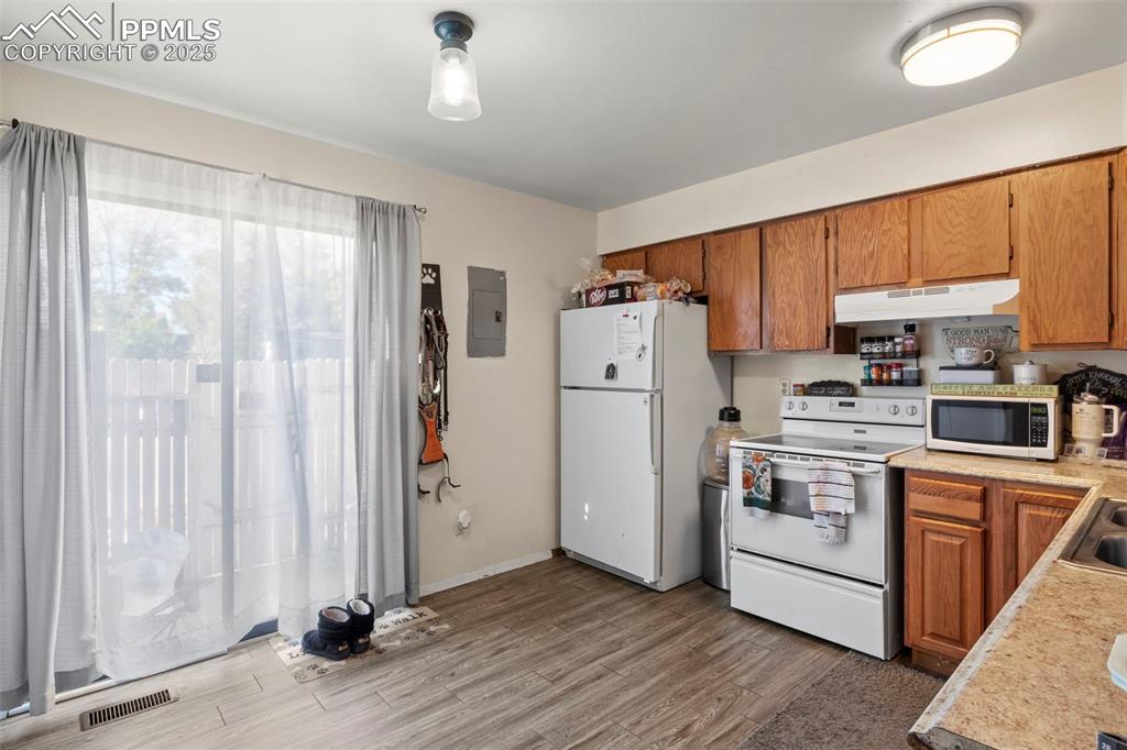 Kitchen featuring light countertops, brown cabinetry, white appliances, light wood-style floors, and under cabinet range hood
