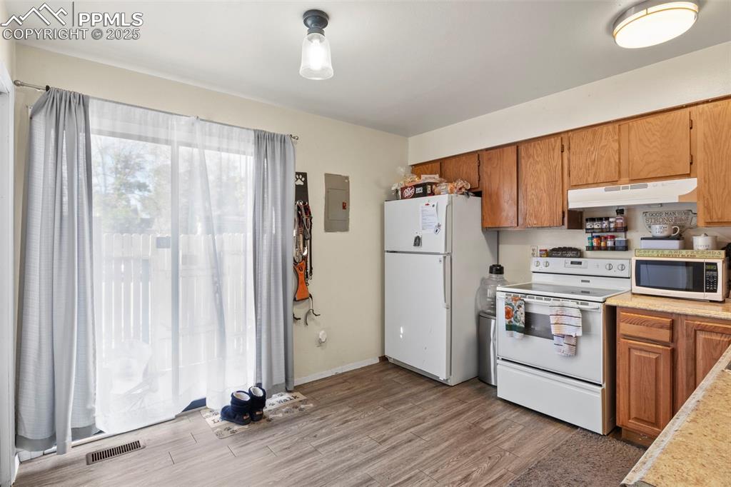 Kitchen featuring brown cabinetry, light countertops, white appliances, light wood-style flooring, and under cabinet range hood