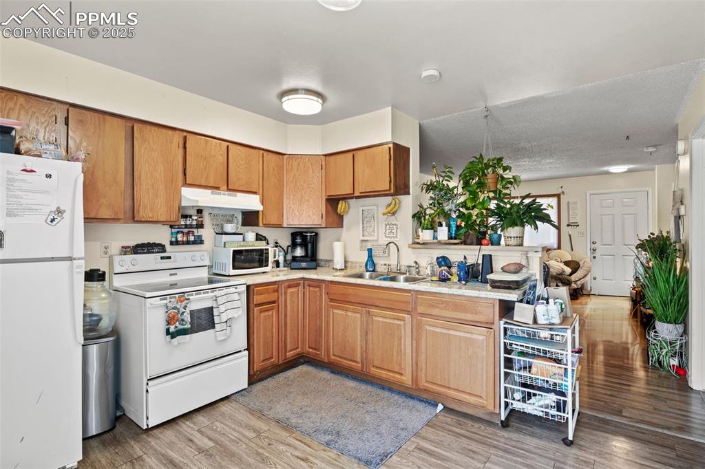 Kitchen with white appliances, light wood-style flooring, brown cabinetry, under cabinet range hood, and a peninsula