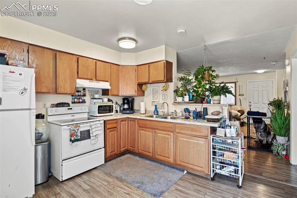 Kitchen featuring white appliances, brown cabinets, light wood-type flooring, under cabinet range hood, and a peninsula