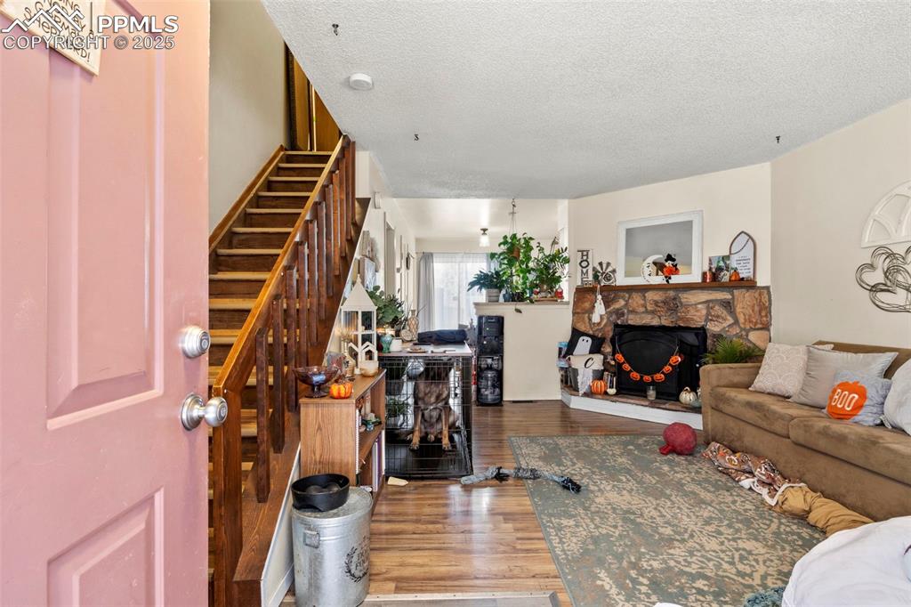 Living room featuring wood finished floors, a textured ceiling, a stone fireplace, and stairs