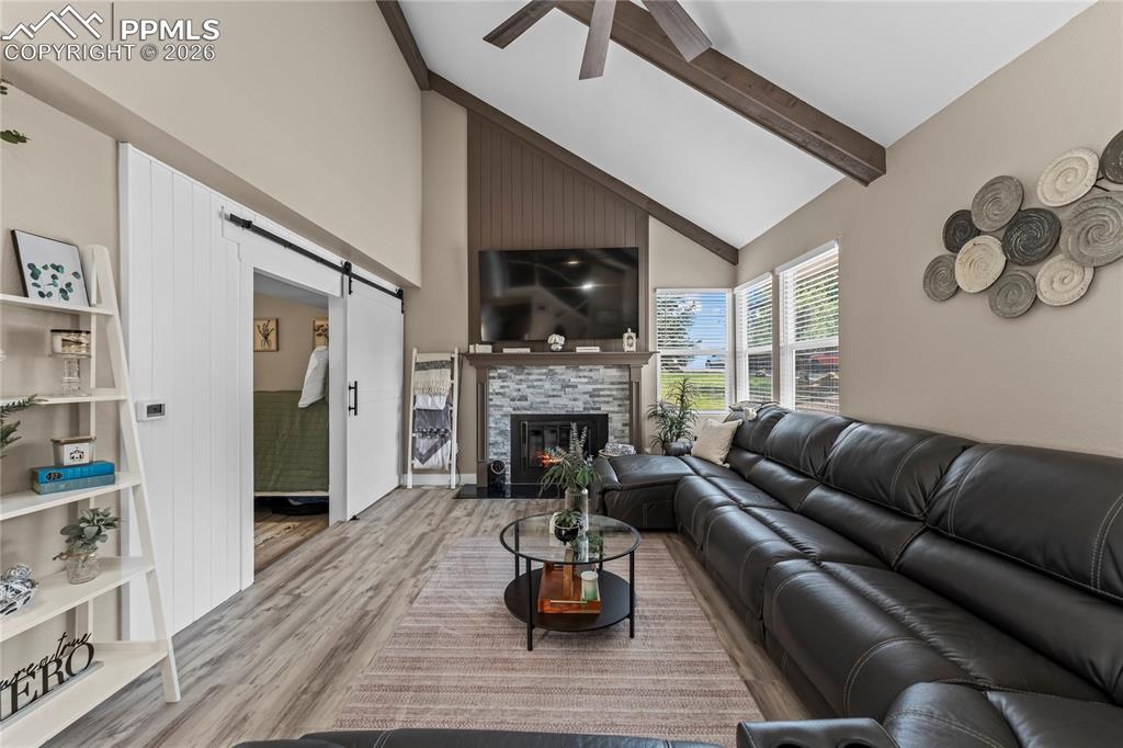 Living area with a barn door, high vaulted ceiling, wood finished floors, a tiled fireplace, and beam ceiling