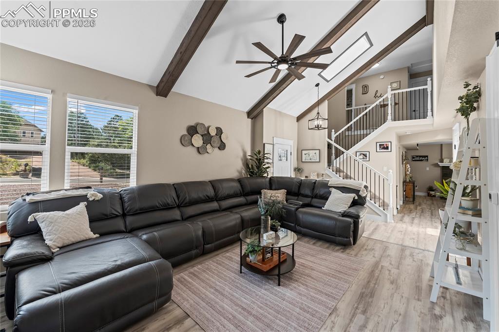 Living area featuring a ceiling fan, beamed ceiling, high vaulted ceiling, and wood finished floors