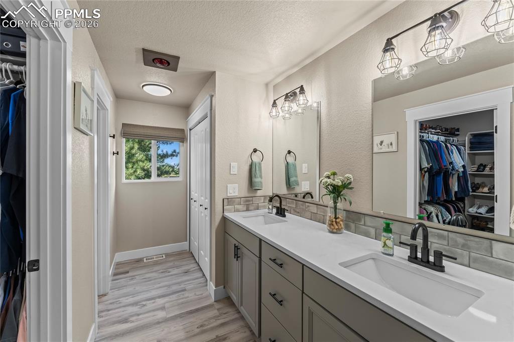 Bathroom with double vanity, a textured ceiling, a walk in closet, wood finished floors, and tasteful backsplash
