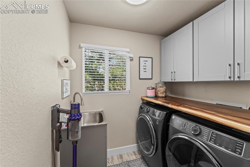 Washroom featuring washer and dryer, cabinet space, a textured wall, and light wood finished floors