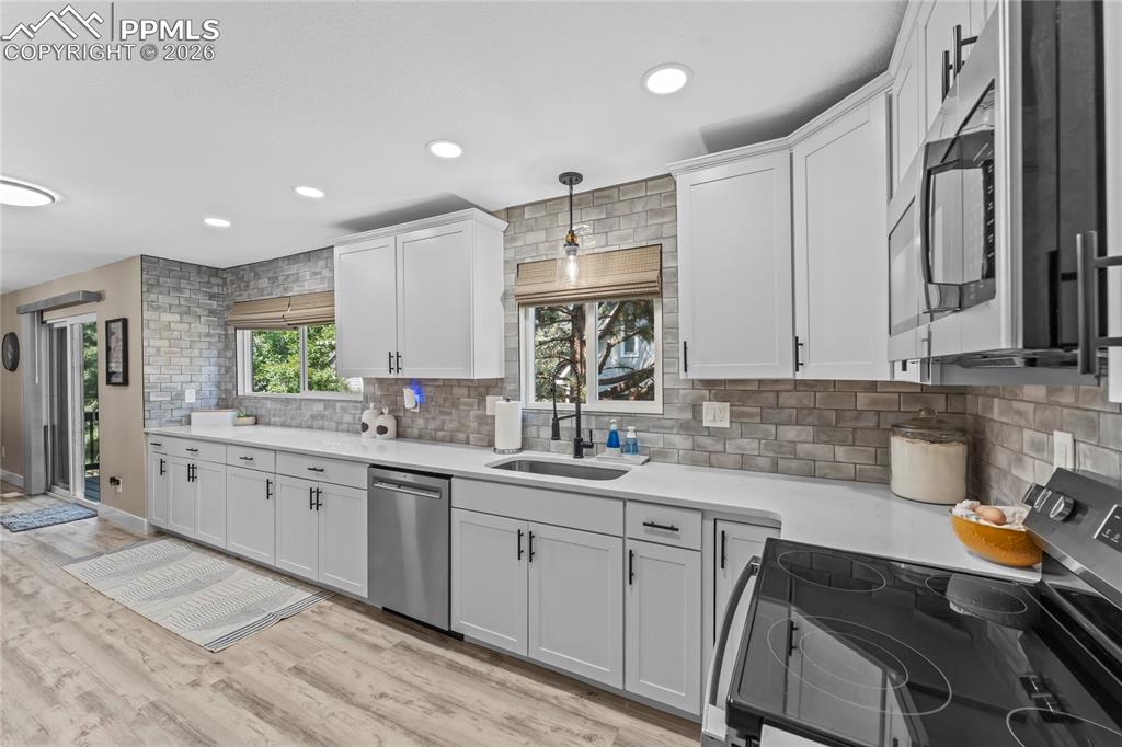 Kitchen featuring stainless steel appliances, tasteful backsplash, light countertops, light wood-style floors, and pendant lighting