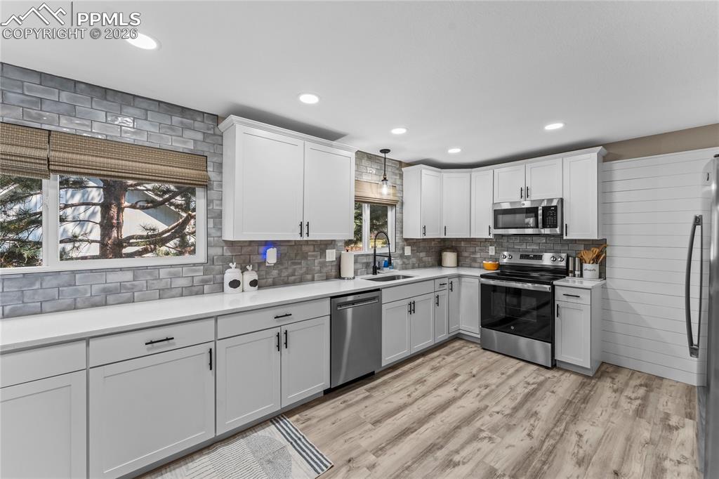 Kitchen featuring appliances with stainless steel finishes, recessed lighting, light wood-style flooring, light countertops, and white cabinetry