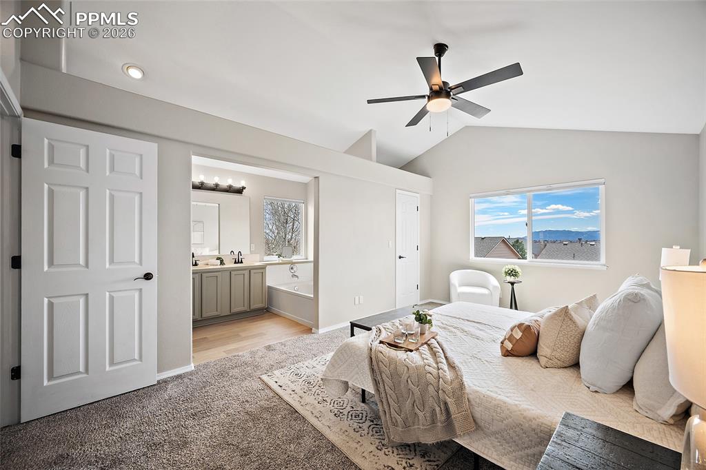 Bedroom with light carpet, vaulted ceiling, ceiling fan, and ensuite bathroom