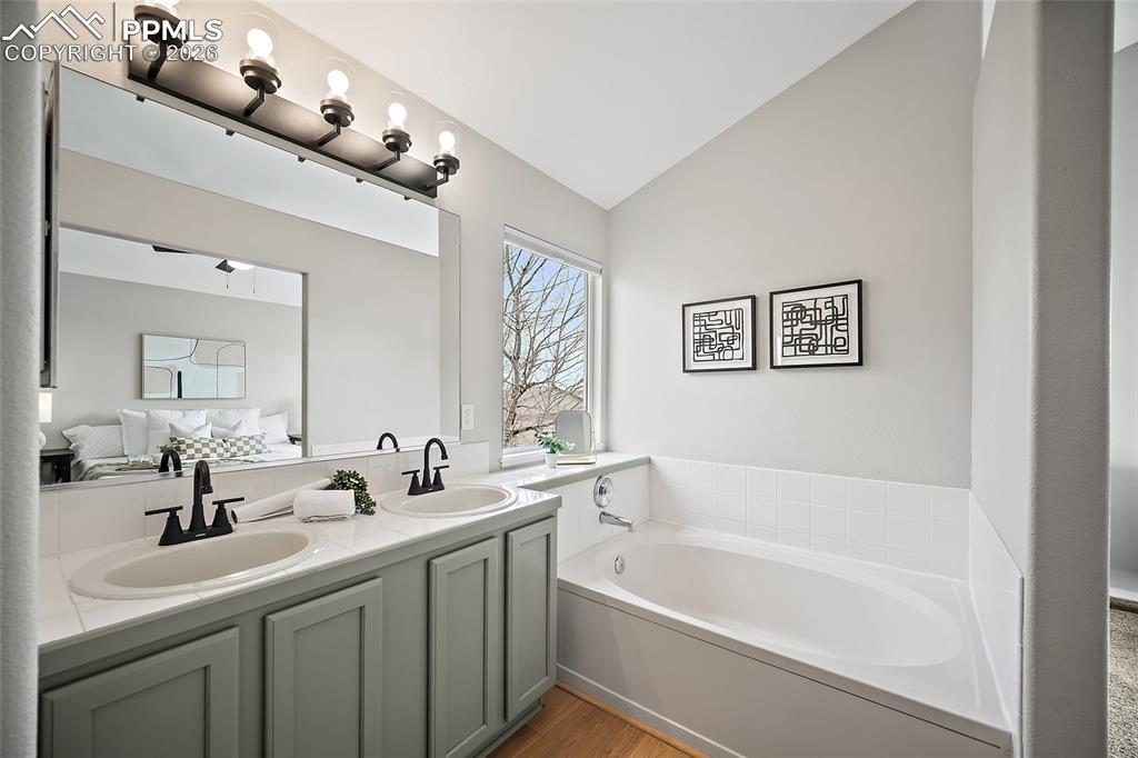 Full bathroom with double vanity, vaulted ceiling, a bath, light wood-style floors, and ensuite bath