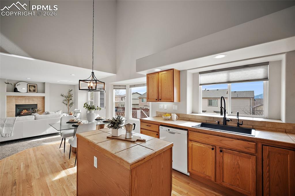 Kitchen featuring tile countertops, a tile fireplace, white dishwasher, open floor plan, and light wood-type flooring
