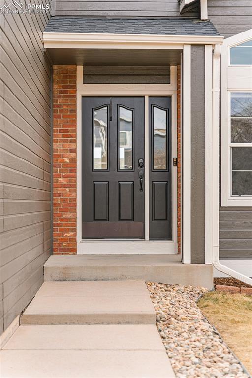 View of exterior entry featuring roof with shingles and brick siding