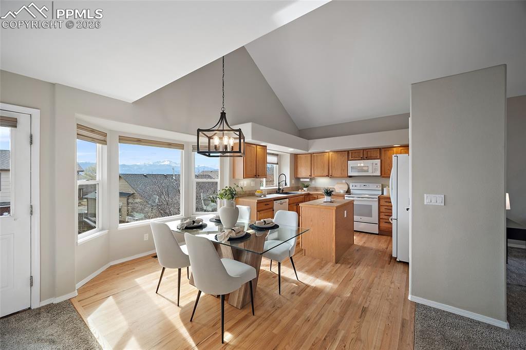 Dining space with a chandelier, vaulted ceiling, light wood-style floors, and healthy amount of natural light