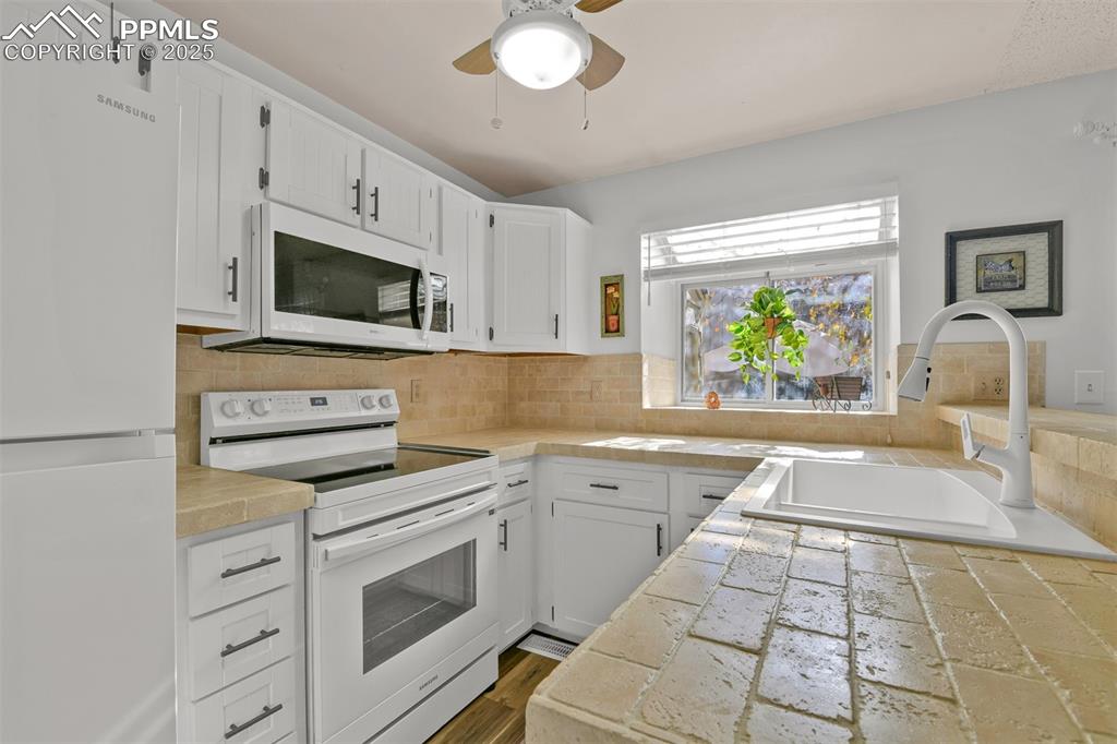Kitchen featuring white appliances, white cabinetry, a ceiling fan, and tasteful backsplash