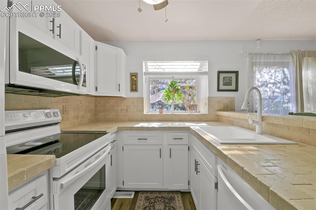 Kitchen with white appliances, white cabinetry, and plenty of natural light