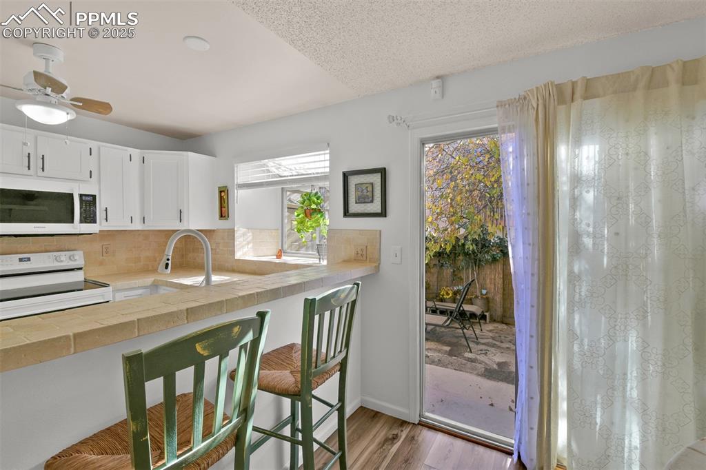 Kitchen with white appliances, white cabinets, tasteful backsplash, light wood-style flooring, and tile countertops