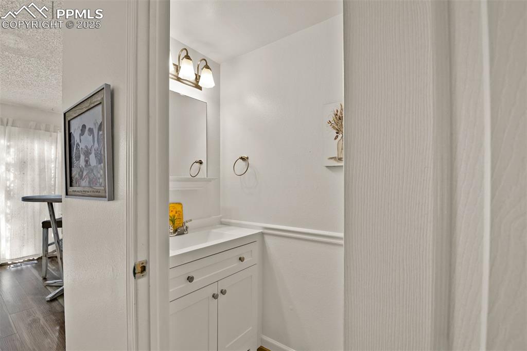 Half bath on the main level with vanity, a textured ceiling, and wood-style flooring