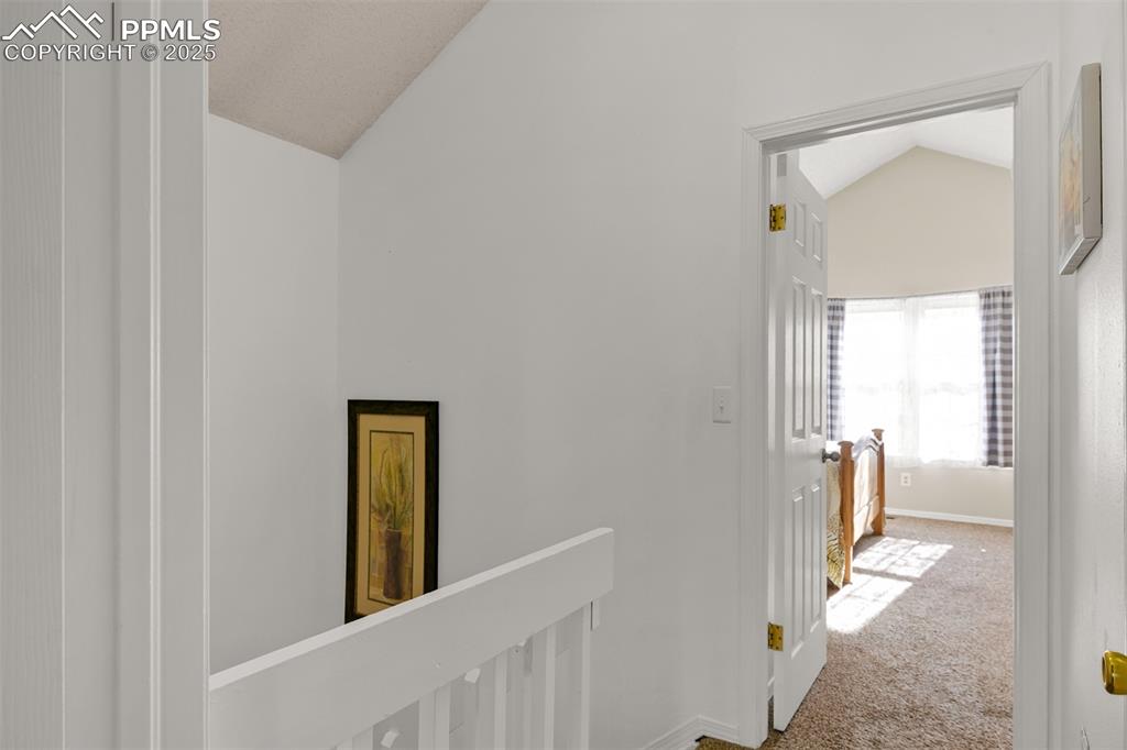Hall on upper level featuring lofted ceiling, carpet flooring, and an upstairs landing