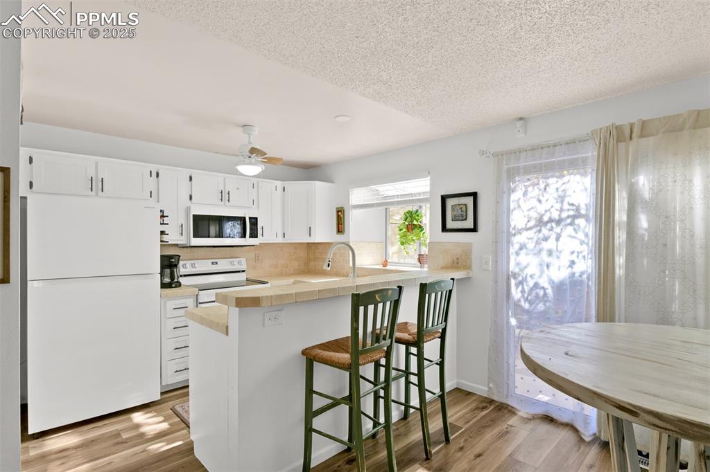 Kitchen on the main level with white appliances, white cabinetry, a breakfast bar area, a textured ceiling, and light wood-style floors
