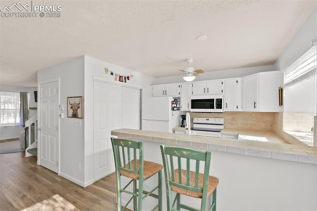 Kitchen featuring plenty of natural light, white appliances, white cabinetry, a peninsula, and a textured ceiling