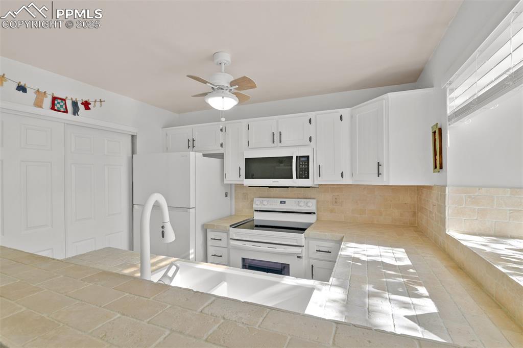 Kitchen with tile counters, white appliances, white cabinets, ceiling fan, and backsplash
