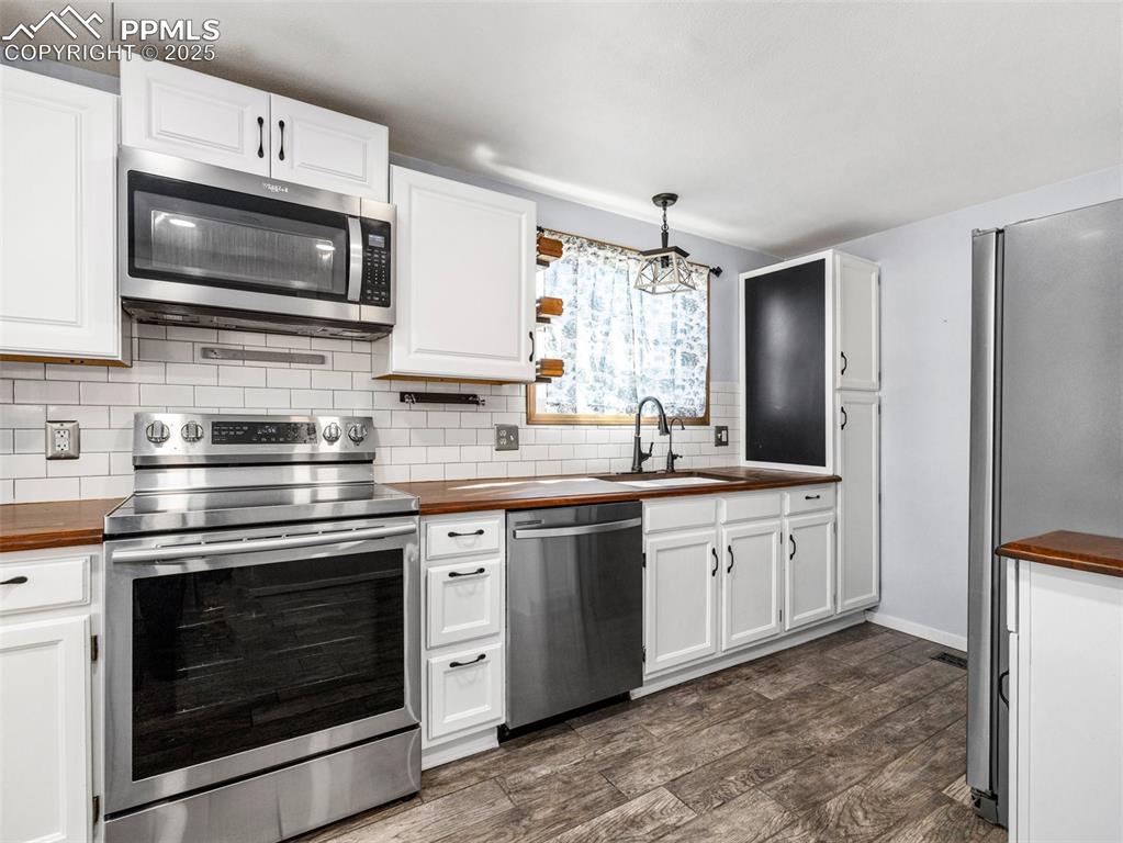 Kitchen with wooden counters, appliances with stainless steel finishes, tasteful backsplash, and white cabinetry