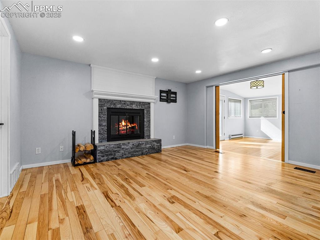 Unfurnished living room with recessed lighting, light wood-type flooring, a stone fireplace, and a baseboard radiator