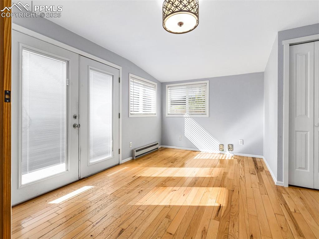 Spare room with lofted ceiling, light wood-style floors, a baseboard heating unit, and french doors