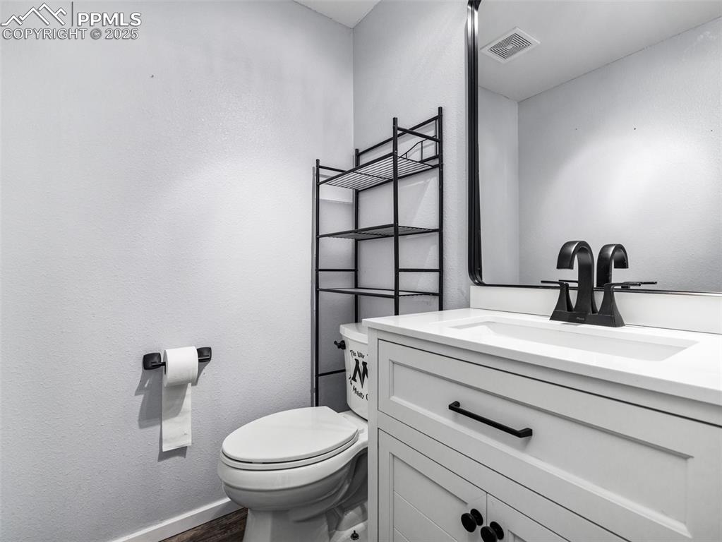 Half bathroom with a textured wall, vanity, and dark wood-style floors