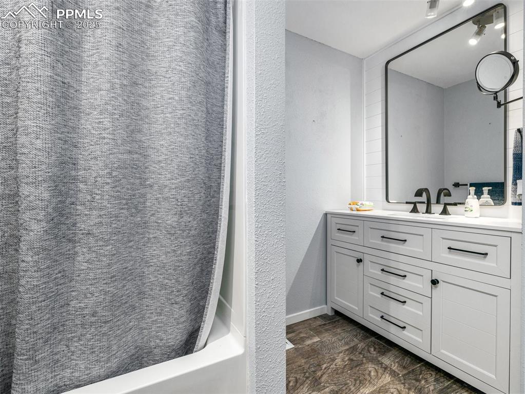 Bathroom featuring vanity, a textured wall, and shower / bathtub combination with curtain