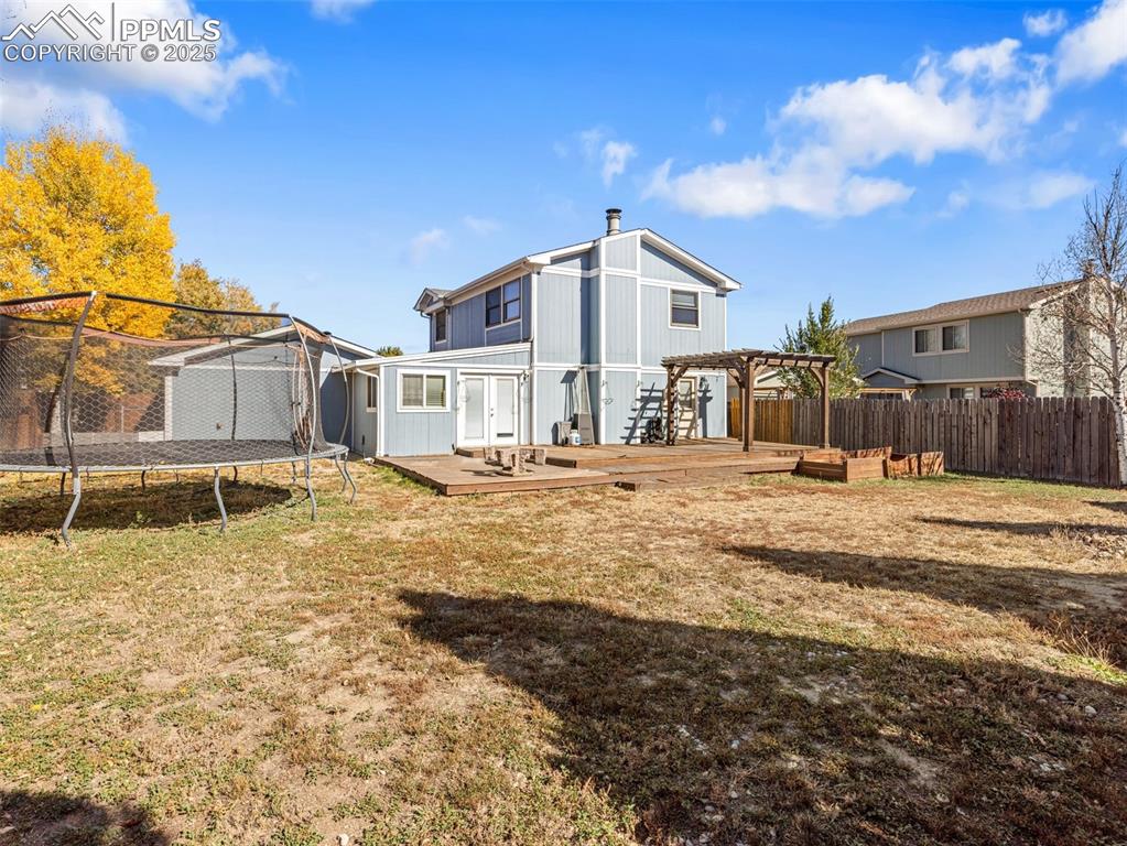 Rear view of house featuring a trampoline, a fenced backyard, and a deck