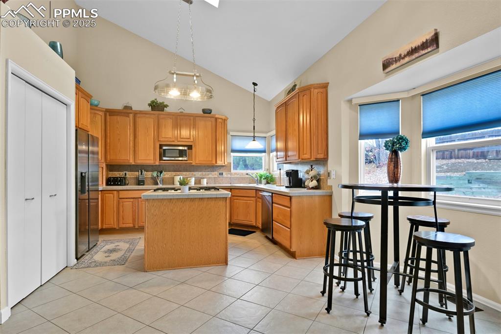 Kitchen featuring a kitchen island, high vaulted ceiling, backsplash, light countertops, and decorative light fixtures