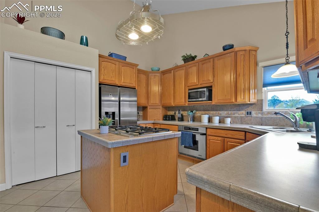 Kitchen featuring appliances with stainless steel finishes, light tile patterned floors, decorative light fixtures, and brown cabinetry