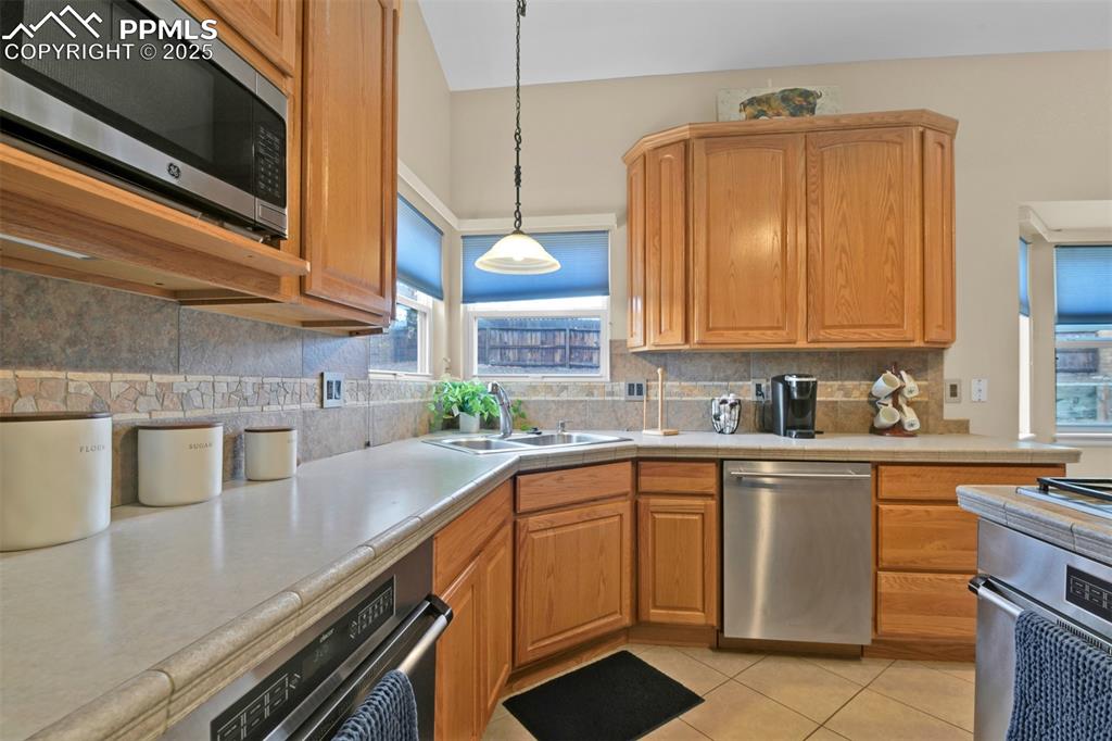 Kitchen with stainless steel appliances, decorative light fixtures, light tile patterned floors, decorative backsplash, and brown cabinetry