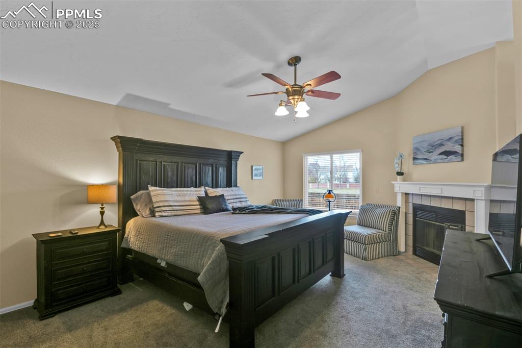 Carpeted bedroom featuring lofted ceiling, a fireplace, and a ceiling fan