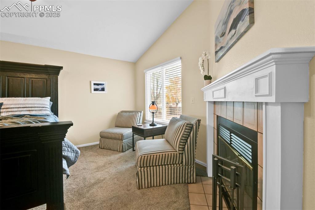 Bedroom with lofted ceiling, light carpet, a tile fireplace, and light tile patterned flooring