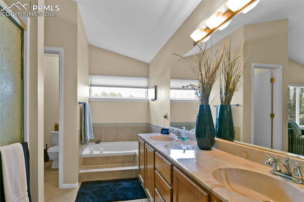 Bathroom featuring vaulted ceiling, double vanity, light tile patterned flooring, a garden tub, and an enclosed shower