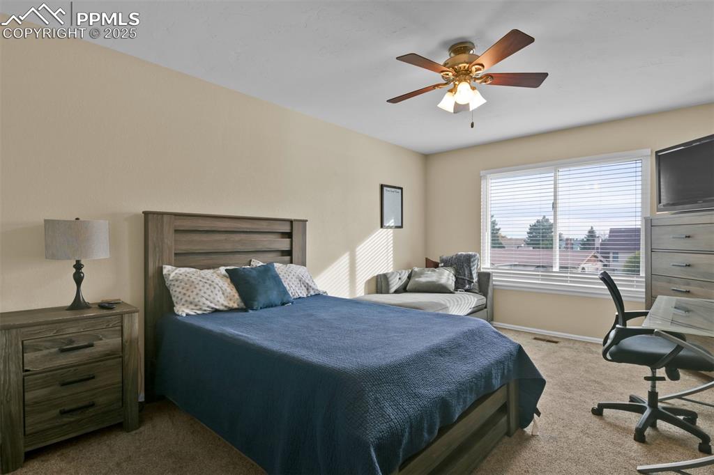 Carpeted bedroom featuring ceiling fan and a desk