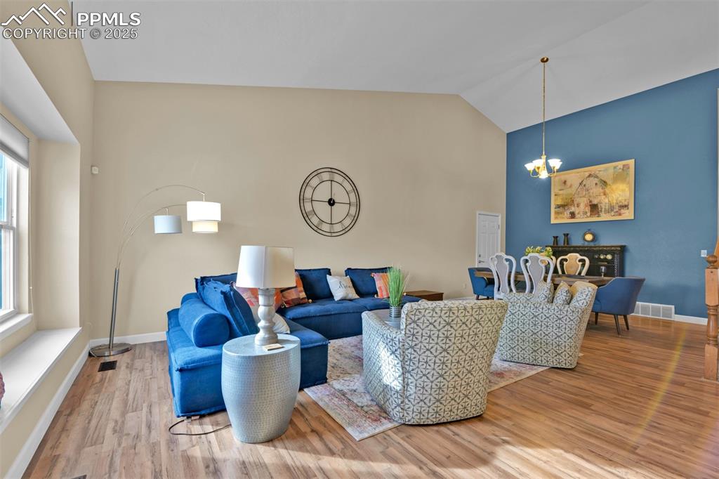Living room with wood finished floors, a chandelier, and vaulted ceiling