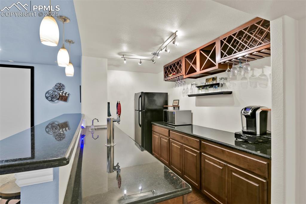 Wetbar with a breakfast bar area, open shelves, dark stone counters, and freestanding refrigerator