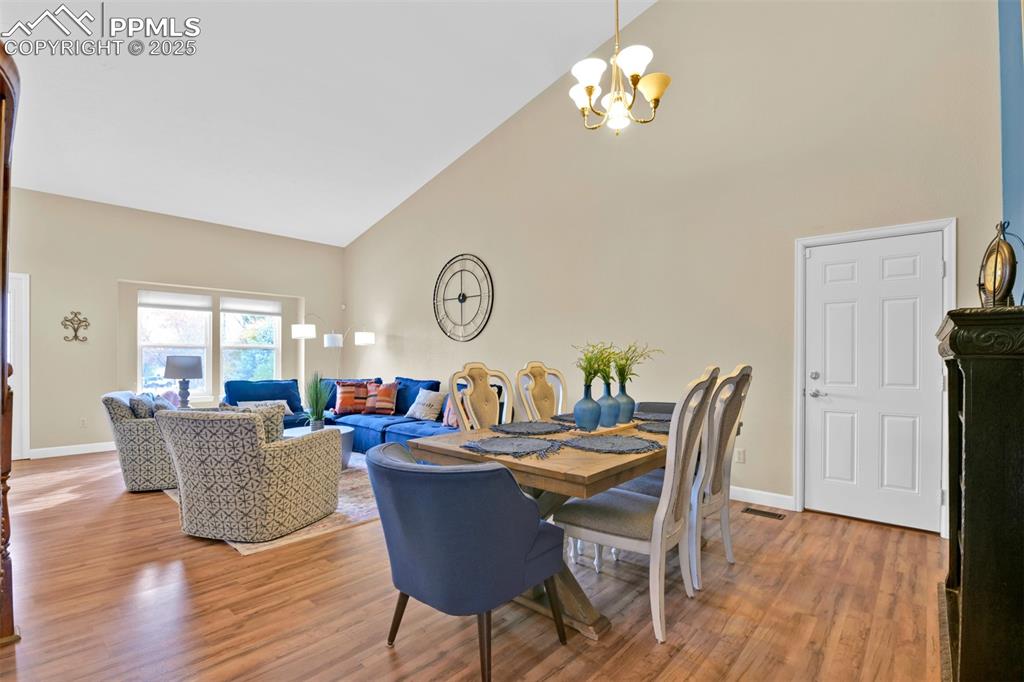 Dining area with high vaulted ceiling, light wood-style flooring, and a chandelier