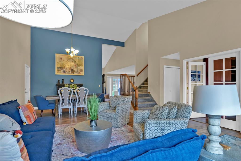 Living area with high vaulted ceiling, wood finished floors, stairway, and a chandelier