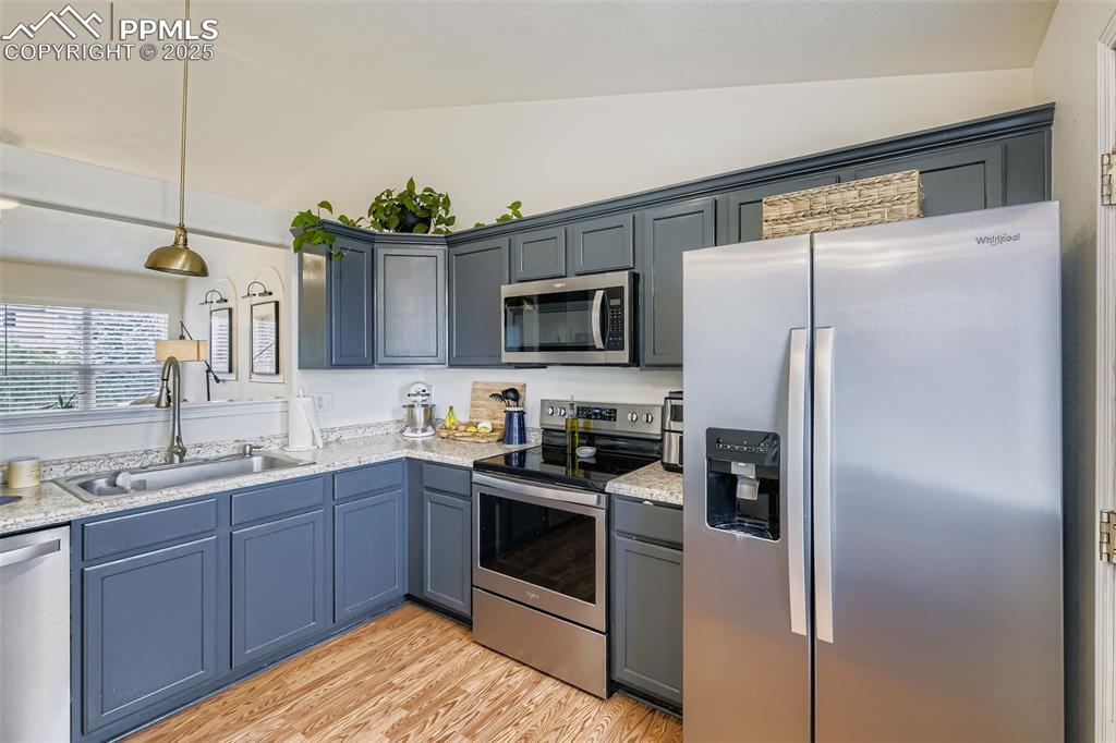 Kitchen featuring appliances with stainless steel finishes, light wood-type flooring, decorative light fixtures, lofted ceiling, and gray cabinets