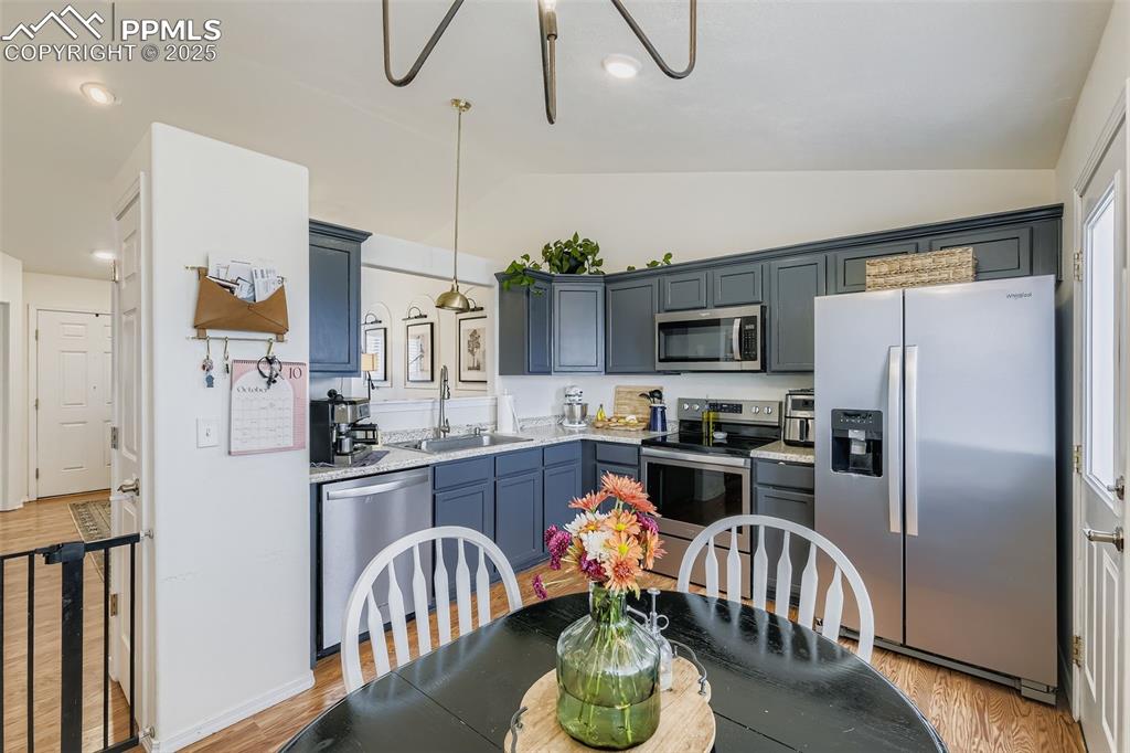 Kitchen with stainless steel appliances, lofted ceiling, light wood-style floors, pendant lighting, and recessed lighting