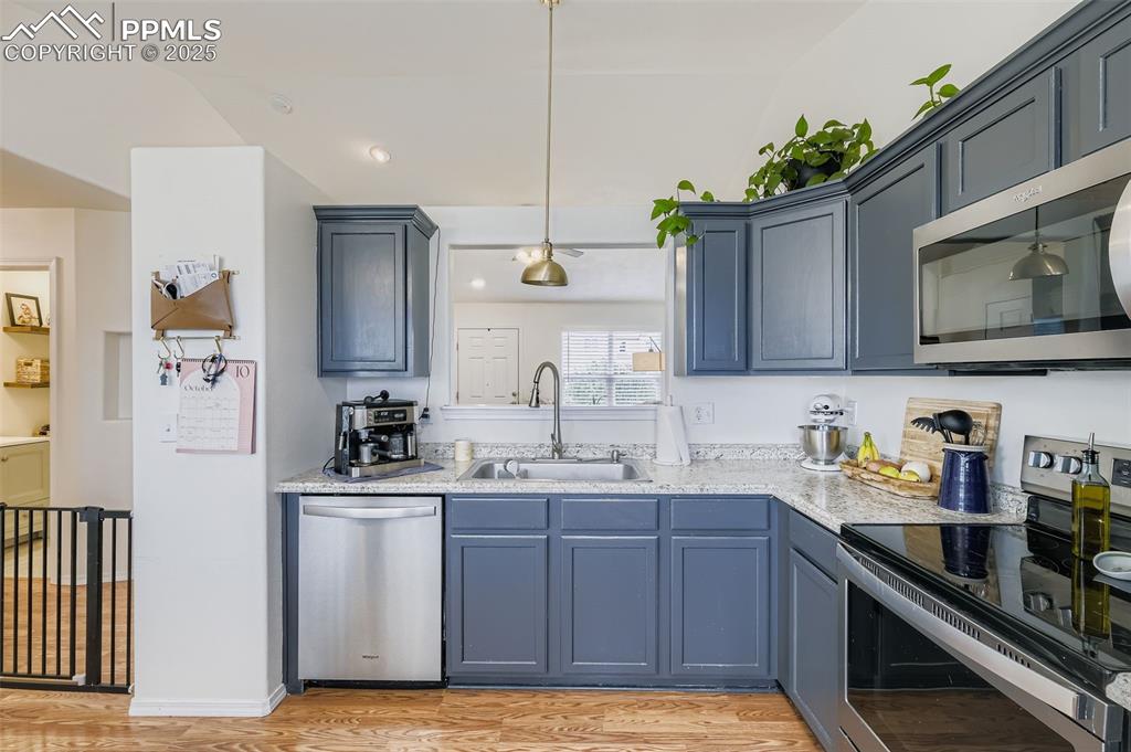 Kitchen with appliances with stainless steel finishes, pendant lighting, light wood-type flooring, blue cabinets, and recessed lighting