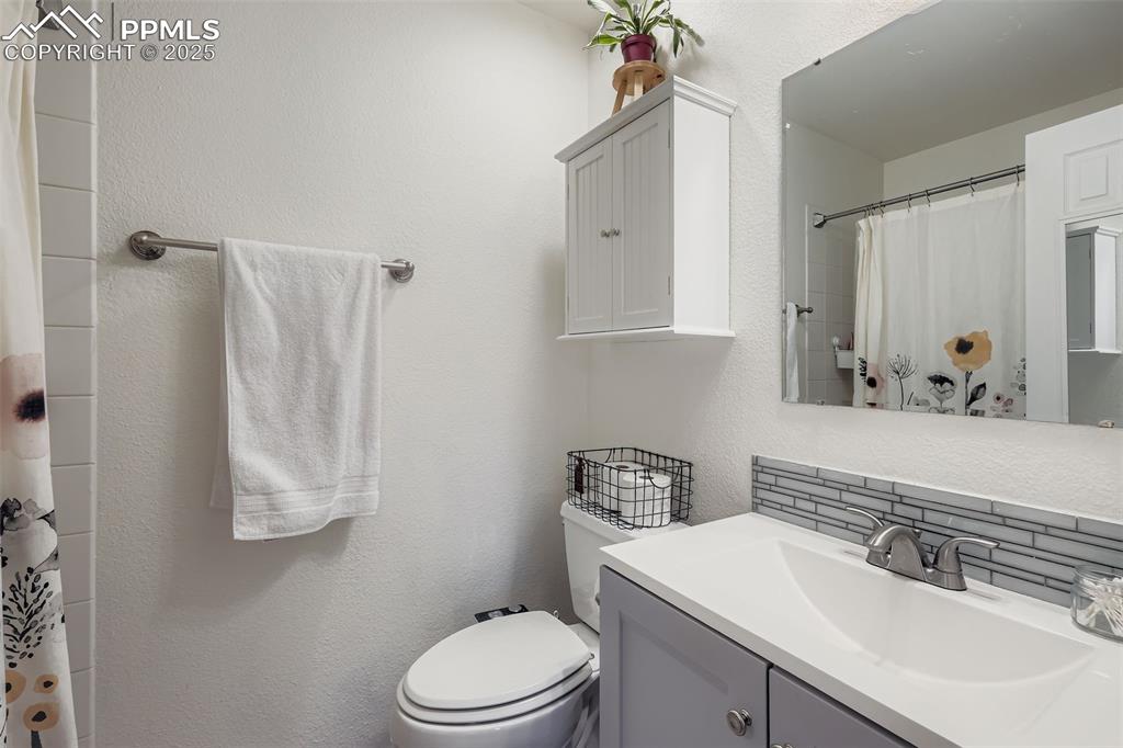 Full bath with a textured wall, a shower with shower curtain, vanity, and decorative backsplash