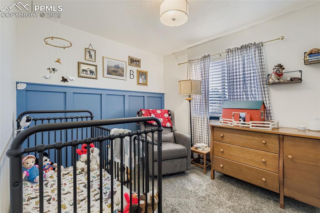 Carpeted bedroom featuring a nursery area and a textured ceiling