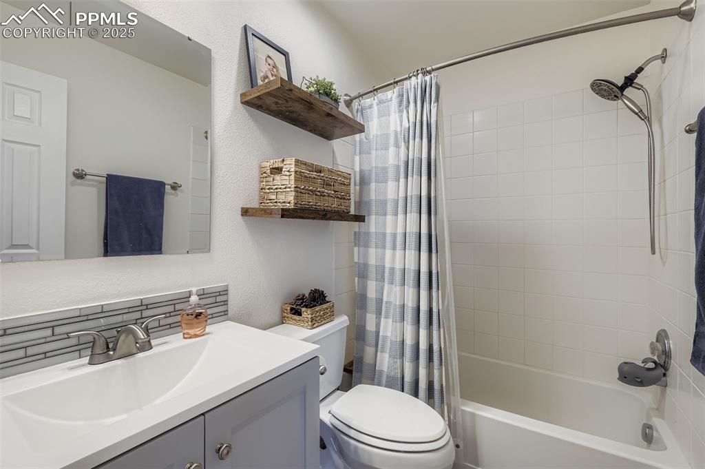 Bathroom featuring a textured wall, shower / bath combo with shower curtain, vanity, and backsplash